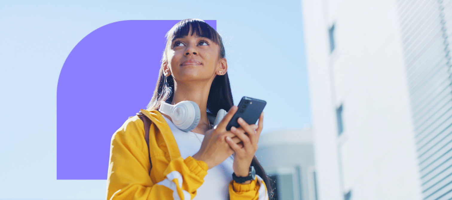 Image of female student in yellow jacket looking upwards while holding mobile phone