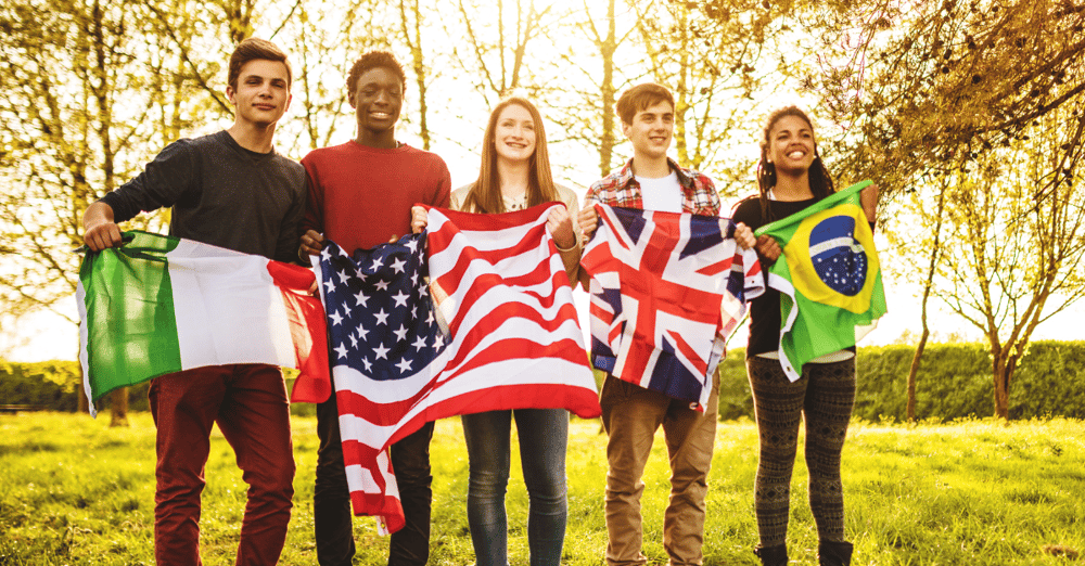 international students holding UK, US, France, and Brazil flags standing in a field