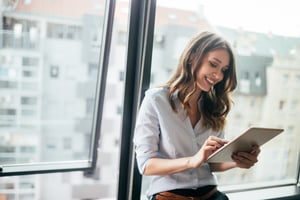 smiling woman in front of window holding an ipad