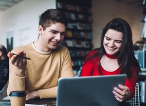 image shows a man and woman looking at a laptop and laughing 