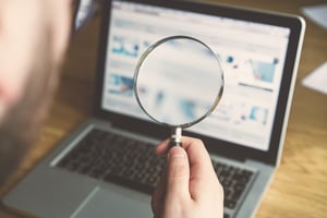 laptop open with hand holding a magnifying glass in the foreground