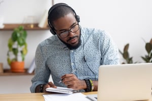 image shows a male student on a laptop while making notes