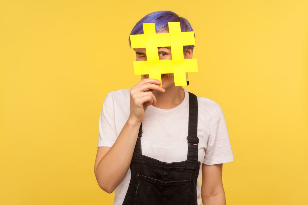 Image shows a woman with a hashtag across her face on a yellow background