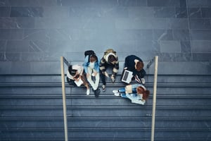 image shows students sitting around a laptop on steps outside 