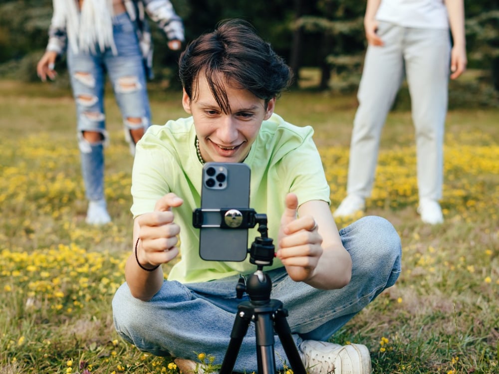 image shows a male student with an iPhone on a tripod getting ready to record a video