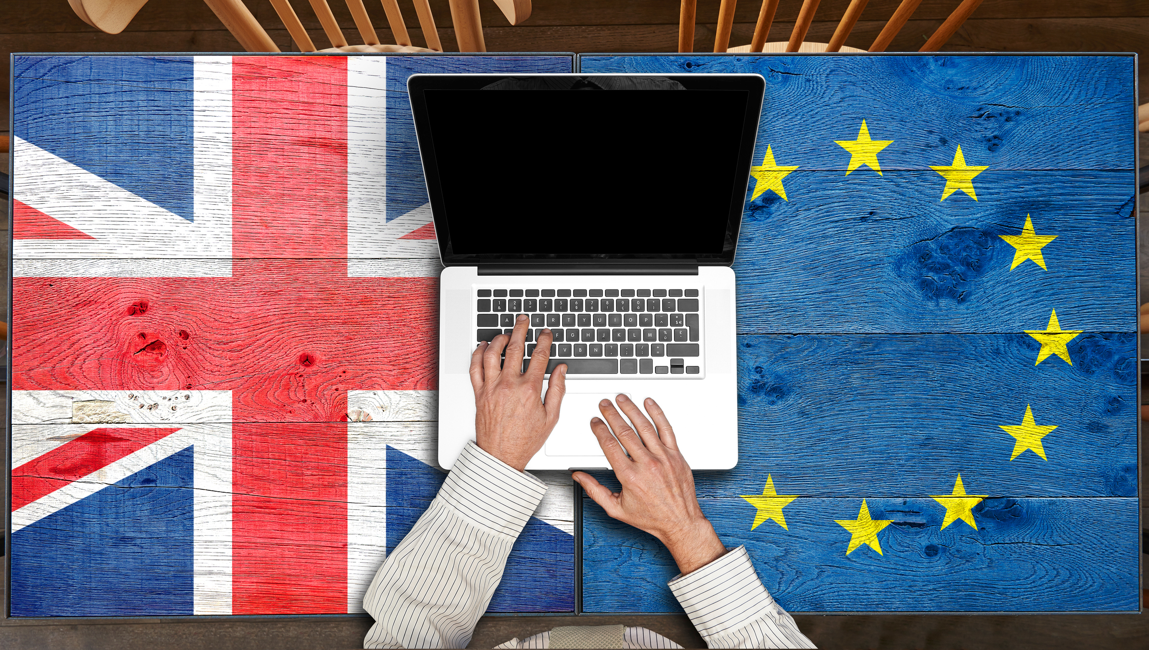 image shows a laptop on top of a Union Jack flag and an EU flag