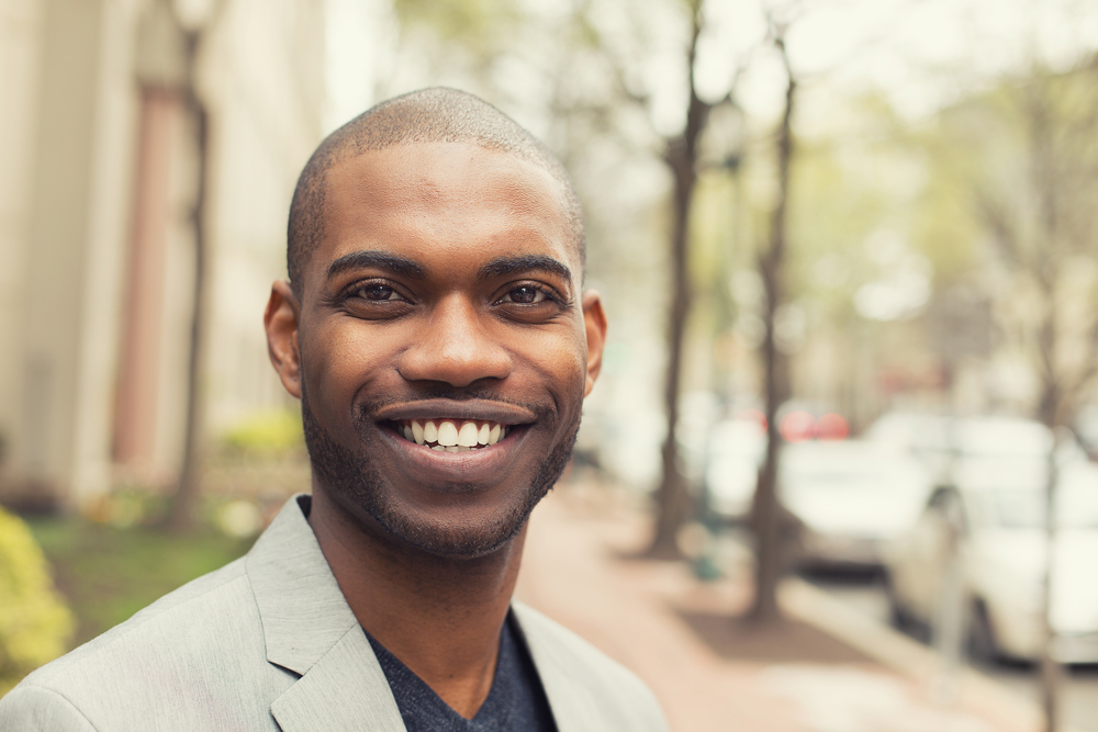 Headshot portrait of young man smiling isolated on outside outdoors background.