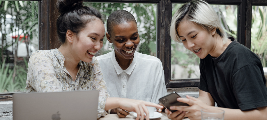 three women looking at something on a mobile phone and laughing