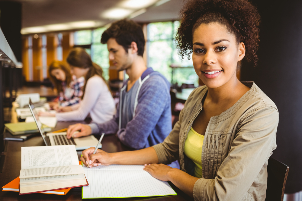 Student looking at camera while studying with classmates in library-1