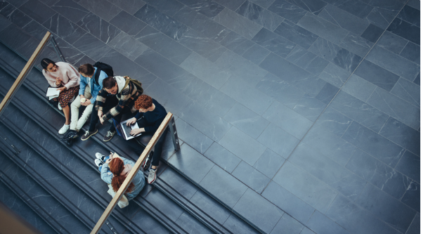 image shows students sitting outside on university steps chatting