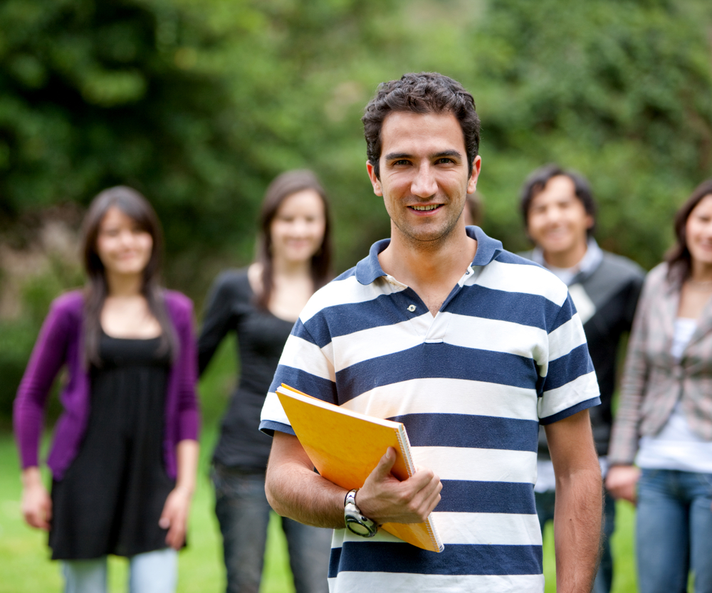 college student smiling outdoors with his friends behind him