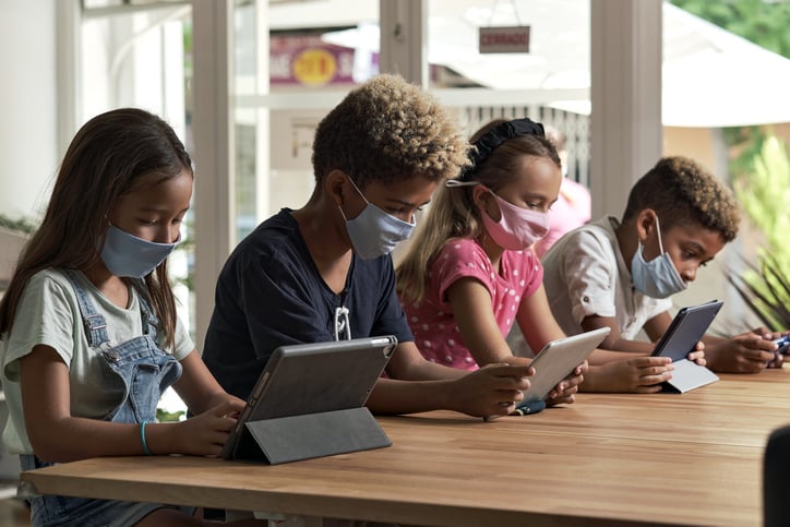 image shows children playing on ipads with face masks on