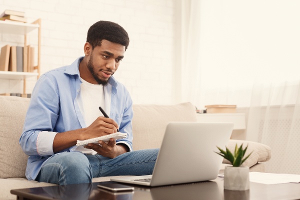 image of student sitting on sofa taking notes with a laptop
